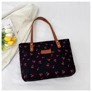 Detail of cherry print canvas tote bag with brown handles and golden rivets on white