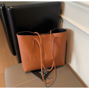Dettaglio borsa tote in pelle caramello con lettere a rilievo e sottili tracolle