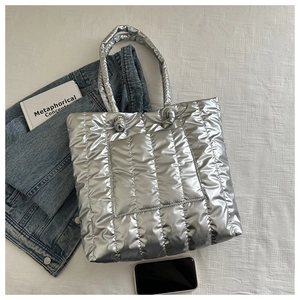 Flat lay of a spacious silver quilted puffer tote bag with metallic finish on white fabric