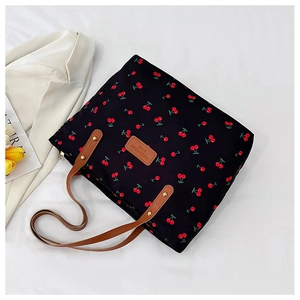 Close-up of black cherry print tote bag with brown leather handles on a white fabric