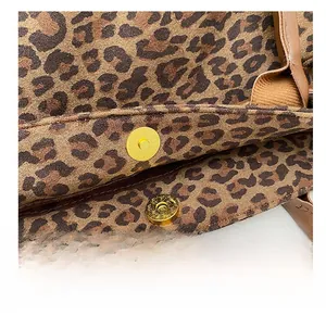 Detail of leopard print fabric featuring a gold magnetic snap and brown leather strap
