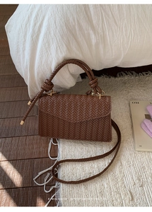 Detail of dark brown woven faux leather handbag with V-shaped flap and braided handle