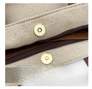Detail shot of the golden magnetic snap button on a beige canvas shoulder bag