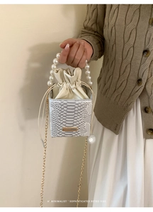 Detail of white snakeskin bucket bag with elegant pearl handle and gold chain strap