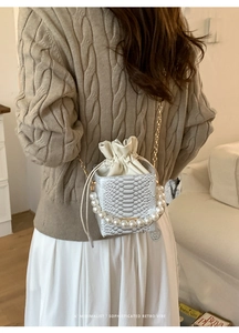 White snakeskin bucket bag with pearl handle and gold chain strap shown on model
