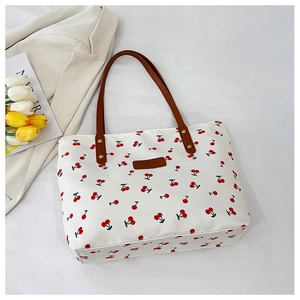 Detailed view of canvas tote bag featuring red cherry prints and brown leather handles