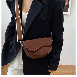 Détail du sac selle marron mat avec bandoulière large et boucles métalliques dorées