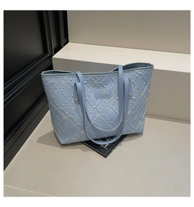 Close-up of light blue pleated tote bag with white floral embroidery and gold logo