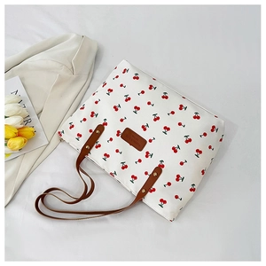 Detail of white cherry print tote bag featuring brown leather handles and gold rivet accents