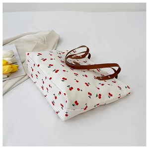 Detail of cherry print tote bag featuring brown leather handles and canvas texture