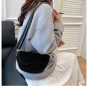 Black saddle crossbody bag with striped wide strap worn by a model in a modern room