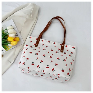 Detail of white cherry print tote bag with brown leather handles and metal rivets