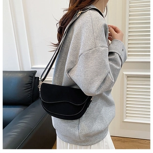 Detail of black saddle bag featuring a striped wide strap and matte finish on model