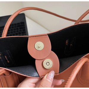 Vista macro della borsa tote in pelle marrone con chiusura magnetica dorata e punti a mano