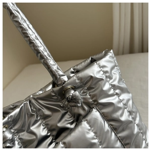 Detailed macro view of metallic silver quilted fabric and knotted handle on puffer tote