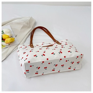 Detail of white cherry print tote bag with brown leather handles and metal rivets