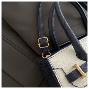 Dettaglio della trama in pelle litchi e fibbia dorata su una borsa blu navy e bianca