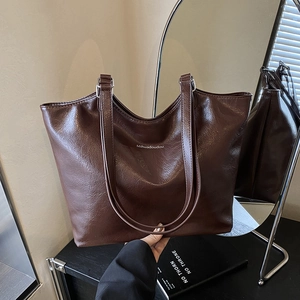 Large dark brown tote bag in oily leather texture with brand name and long handles