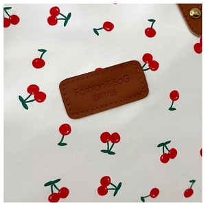 Close-up of the cherry print pattern and embossed brown leather label on the white tote bag