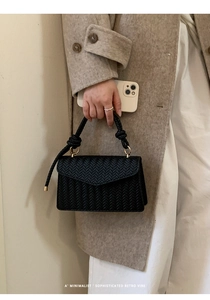 Detail of black woven texture handbag with unique knotted handle and metallic rings