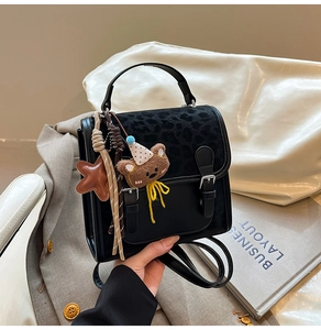 Close-up of black leather bag with leopard print flap and cute bear charm detail