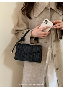 Detail of black woven shoulder bag with knotted handle and metallic ring on model