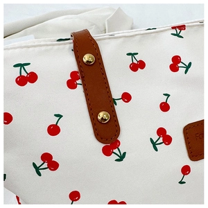 Detail view of canvas tote bag showing cherry print, leather logo patch, and golden rivets
