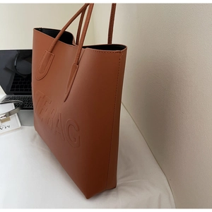 Dettaglio macro della borsa tote marrone con scritta THE BAG a rilievo e manico