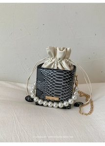 Detail of snakeskin texture, pearl chain handle and gold hardware on a bucket bag