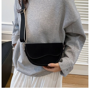 Close-up of black matte saddle bag with stylish wide shoulder strap and gold hardware