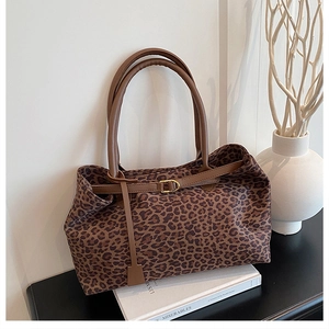 Detail of leopard print tote bag with brown leather handles and gold buckle on a book