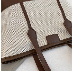 Close-up of off-white canvas tote with deep brown leather trim and reinforced stitching