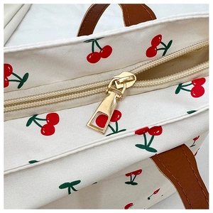 Detail of golden metal zipper and brown leather handles on cherry print tote bag