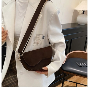 Close-up of retro saddle bag featuring wavy flap design and wide woven strap on a white blazer