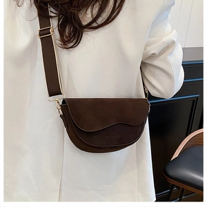 Détail du sac de selle demi-cercle marron foncé avec large bandoulière sur blazer blanc