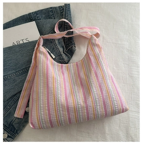 Détail d'un sac cabas à rayures colorées en tissu seersucker avec fermeture éclair sur lit blanc