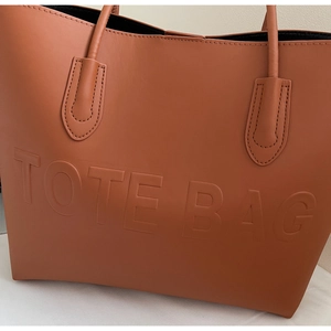 Dettaglio della scritta TOTE BAG in rilievo sulla superficie in pelle marrone ruvida