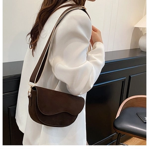 Detail of dark brown matte saddle bag with wavy flap design and bicolor wide strap