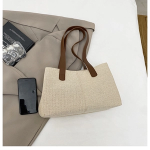 Vista piatta della borsa tote minimalista in tela beige con manici in pelle marrone e decori