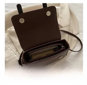 Détail du sac bandoulière marron foncé montrant l'intérieur spacieux et le compartiment zippé