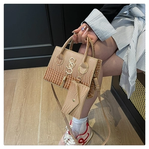 Bolso de mano marrón con textura de cocodrilo, detalles dorados, borlas y charm de sobre