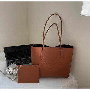Detail of a brown leather tote bag set with embossed lettering and matching small pouch