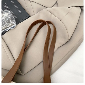 Dettaglio dei manici in pelle marrone e trama intrecciata beige di una borsa vintage