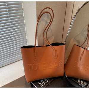 Dettaglio borsa tote in pelle caramello con scritte in rilievo e tracolle sottili