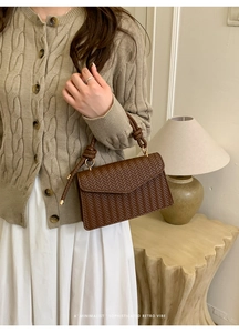 Detail of dark brown woven handbag with knotted handle and elegant gold metal hardware