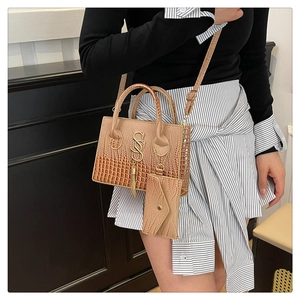 Bolso marrón con relieve de cocodrilo, logotipo dorado y detalle de borla