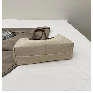 Dettaglio della borsa tote beige intrecciata con manici marroni e base strutturata