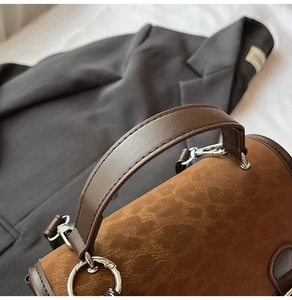 Detail of suede textured handbag with dark leather handle and silver metal ring buckle