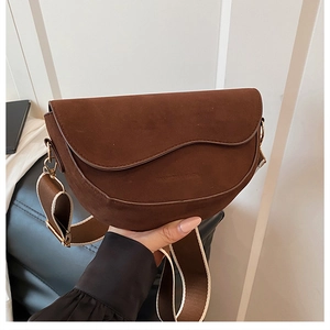 Detail of dark brown suede saddle bag with wavy edge flap and striped strap