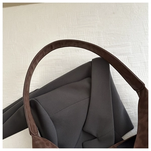 Detail view of deep brown suede shoulder bag strap against a grey blazer for a chic look